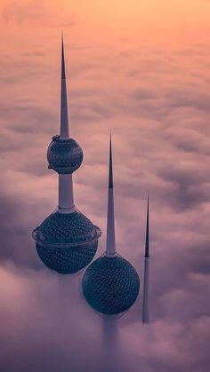 two tall buildings sitting above the clouds at sunset