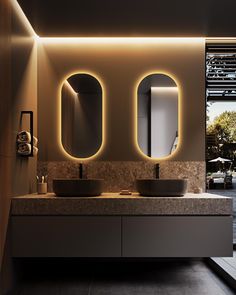 a bathroom with two sinks, mirrors and lights on the wall above them is lit up at night