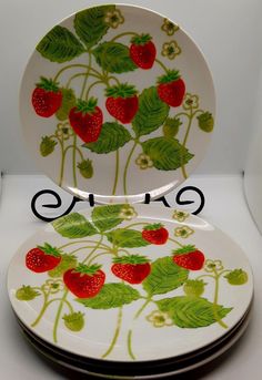 two plates with strawberries painted on them are stacked next to each other in front of a white background