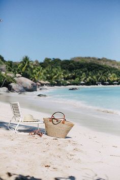 a white chair sitting on top of a sandy beach next to the ocean and palm trees