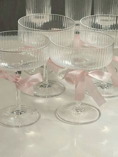 four wine glasses with pink bows on them sitting on a white tableclothed surface