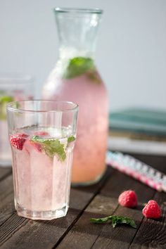 two glasses filled with ice and raspberries on top of a wooden table next to a