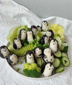 a plate full of sushi and vegetables with penguins on them, sitting on a white cloth