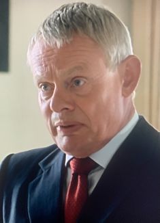 an older man in a suit and tie looking at the camera while wearing a red tie