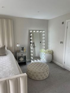 a bedroom with a round ottoman and large mirror in the corner, along with lights on the wall