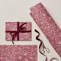 a pair of scissors next to a pink wrapping paper with a red ribbon on it