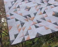 a quilted table topper sitting on the side of a tree in front of some trees