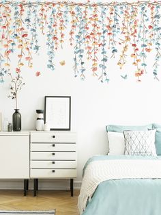 a bed room with a neatly made bed next to a wall covered in colorful flowers