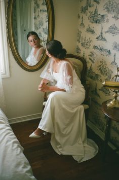 a woman sitting on a chair in front of a mirror with another person looking at her reflection