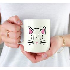 a woman holding a white coffee mug with a cat face on it's side