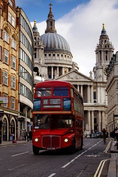 a red double decker bus driving down a street next to tall buildings with domes on top