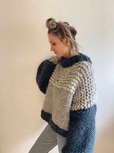 a woman standing in front of a white wall wearing a blue and grey knit sweater