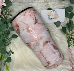 the pink marble tumbler is next to flowers and greenery on a white fur surface