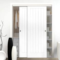 a white closet with two doors open and some vases on the floor next to it