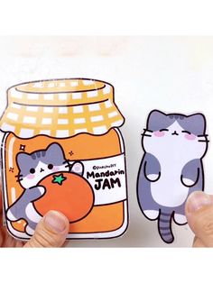 a person holding up a sticker next to a jar of orange jam with two cats on it