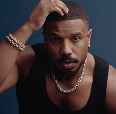 a man wearing a black tank top and silver chains around his neck is looking at the camera