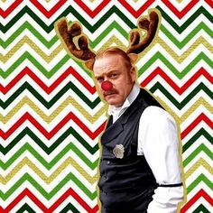 a man with a red nose and reindeer antlers on his head is standing in front of a chevron background