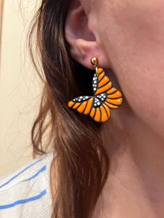 a close up of a person wearing earrings with an orange butterfly on it's ear