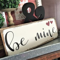 a wooden sign that says be mine on top of a shelf next to a potted plant