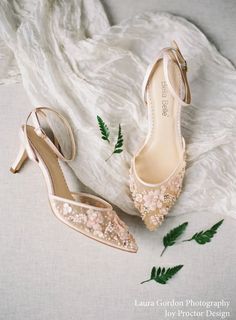 two pairs of shoes sitting on top of a white blanket next to green plant leaves