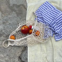 an apple and two oranges are in a bag on the ground next to a towel