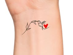 a woman's wrist with a small red heart tattoo on the left side of her arm