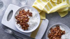 two white bowls filled with rice and chili next to silverware on top of a table