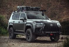 the front end of a gray suv parked on a dirt road with grass and bushes in the background