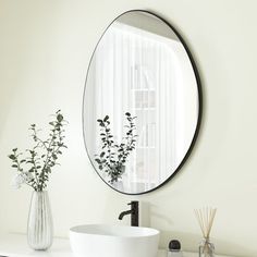 a white sink sitting under a round mirror next to a vase with flowers in it