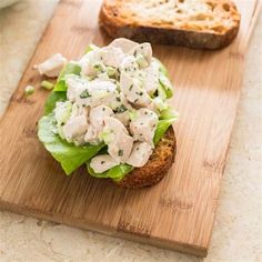 a wooden cutting board topped with lettuce and chicken salad next to a loaf of bread