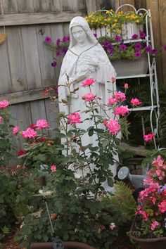 a garden with pink flowers and a statue in the center, surrounded by potted plants