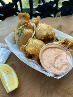 some food is sitting on a table next to a lemon wedge and dipping sauce in a bowl