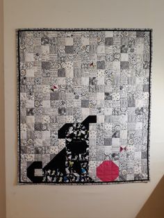 a black dog sitting on top of a patchwork piece of cloth next to a wall