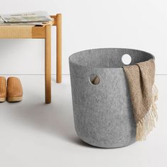 a gray basket sitting on top of a white floor next to a wooden table and chair