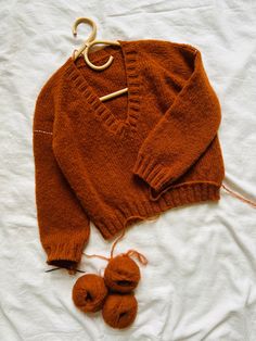 an orange sweater and two balls of yarn are laying on a white sheet with scissors