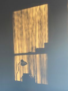 the shadow of a lamp on a window sill in front of a curtained window