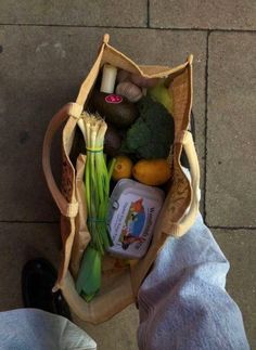 a person is holding a bag full of vegetables and other things to eat on the sidewalk