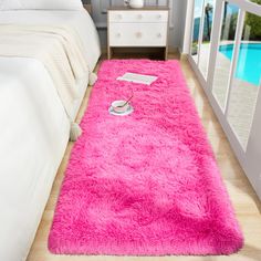 a bright pink shaggy rug on the floor next to a bed