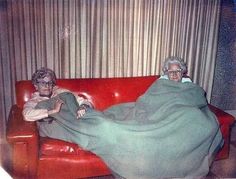 an older woman laying on top of a red couch next to a younger woman in glasses