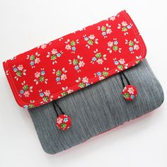 a red and gray purse with flowers on the front is sitting on a white surface