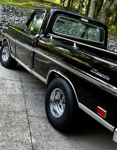 an old black truck parked on the side of the road next to a stone wall