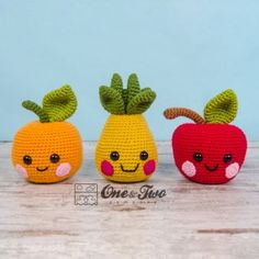 three crocheted apples and two oranges with faces on them sitting next to each other