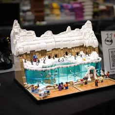 a lego model of a building with penguins in the water and people standing around it