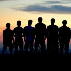 a group of people standing next to each other in front of the sun at sunset