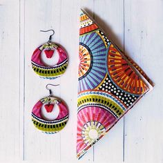 two pairs of earrings and a napkin on a white wooden table with a red strawberry in the center