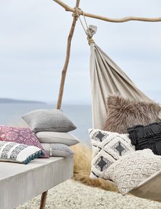 an outdoor hammock with pillows and blankets on it next to the ocean,