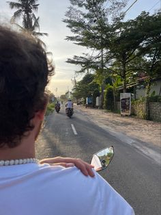 two people riding motorcycles down the street in front of trees and bushes on either side of the road