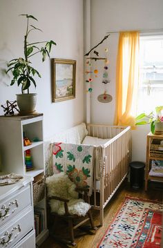 a baby's room with a crib, dresser and potted plant in the corner