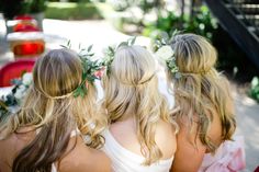 three bridesmaids with flower crowns on their heads looking at the back of them