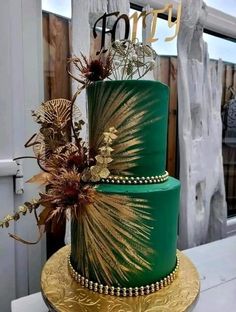 a green and gold wedding cake with flowers on top